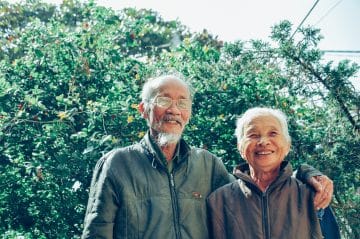 An elderly couple pose in a garden.