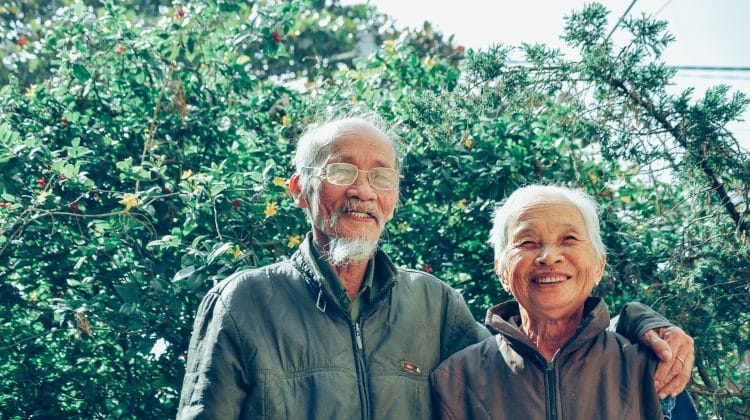 An elderly couple pose in a garden.